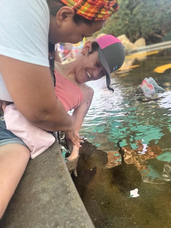 A Big Moves caregiver supporting a client reaching into a stingray touch tank